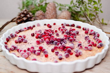 Cake or baked pudding of cottage cheese with red bilberry on white baking dish on wooden background