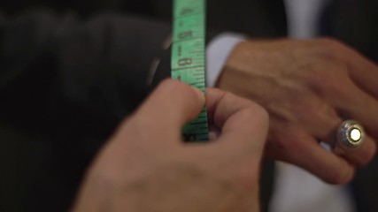 Close-up businessman during fitting in atelier, male hand wearing handmade unfinished suit as tailor taking measures with measuring tape, adjust jacket sleeves for customer size