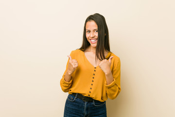 Young hispanic woman against a beige background raising both thumbs up, smiling and confident.