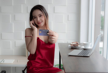 Sexy businesswoman Wearing a red dress. Sitting by the window. Inside the living room There are notebooks and snacks on the table. Talking on the phone about business finance and credit.