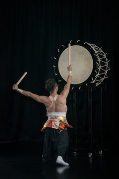 Taiko drummer hits the big drum on stage on a black background, back view.