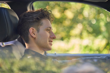 Smiling young driver in car with unsharp greenery in background through window