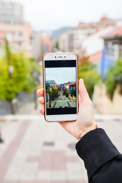 Stock vertical photo of a hand holding a mobile phone where you see the street through the screen