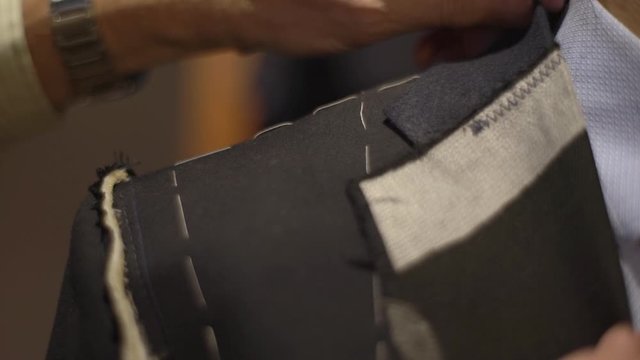 Close-up of man shoulder as tailor taking measures with measuring tape, craftsman pin sleeves and adjust handmade suit during fitting in atelier, businessman order jacket. Fashion concept