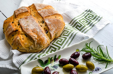 Freshly baked olive bread lying on a cloth with a dish of black and green olive. 