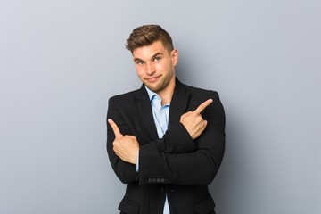 Young handsome caucasian man points sideways, is trying to choose between two options.