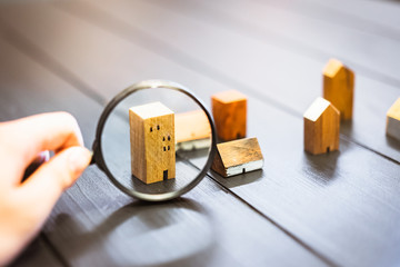 Hand holding magnifying glass and looking at house model, house selection, real estate concept.