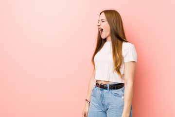 Young redhead ginger woman against a pink wall shouting towards a copy space