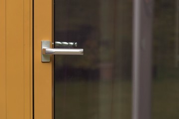 Close up macro view of silver door handle of yellow glass door. Building construction concept. 