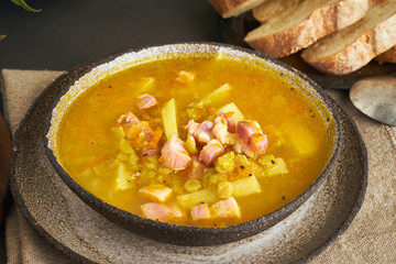 Winter hot soup with chopped green peas, pork, bacon, smoked on dark brown wooden table. Delicious appetizing fat rich soup.