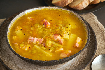 Winter hot soup with chopped green peas, pork, bacon, smoked on dark brown wooden table. Delicious appetizing fat rich soup.
