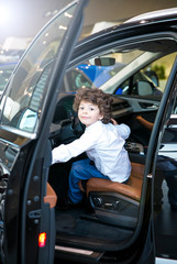 Child observing and testing new car in dealership. Little boy sitting in driver's seat, car cabin. Little boy closing the door with his hand.