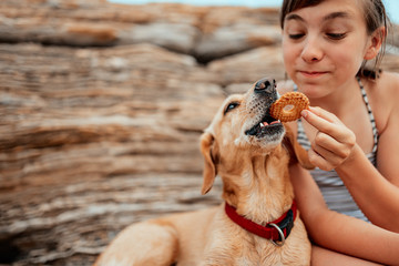 Girl sharing cookies with her dog on the beach
