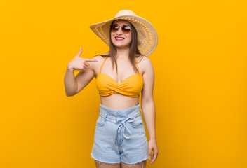 Young caucasian woman wearing a straw hat, summer look person pointing by hand to a shirt copy space, proud and confident