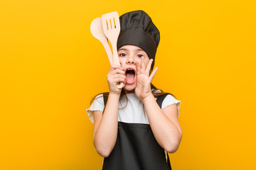 Little caucasian girl wearing a chef costume shouting excited to front.