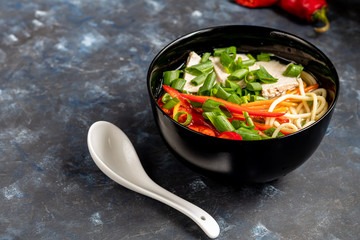 Asian soup with wheat noodles, slices of meat, red chili peppers. Decorated with mint leaves, basil, green onion feathers. There are carrots and broccoli. A healthy, dietary product. Copy space.  