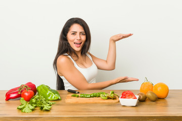 Young curvy woman preparing a healthy meal shocked and amazed holding a copy space between hands.