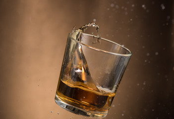falling glass with whiskey and spray on a brown background