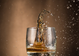 falling glass with whiskey and spray on a brown background