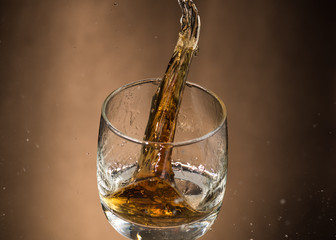 falling glass with whiskey and spray on a brown background