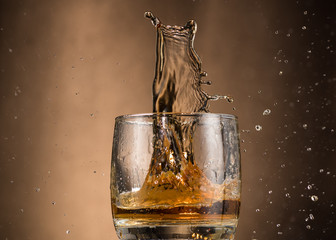 falling glass with whiskey and spray on a brown background
