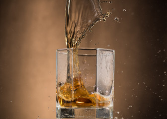 falling glass with whiskey and spray on a brown background