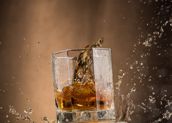 falling glass with whiskey and spray on a brown background