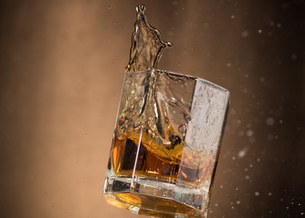falling glass with whiskey and spray on a brown background
