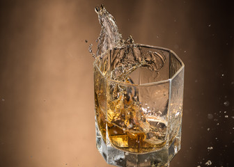 falling glass with whiskey and spray on a brown background