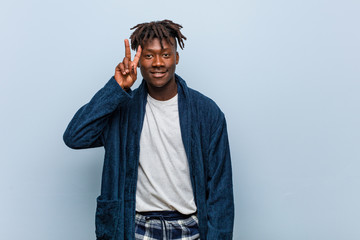 Young african black man wearing pajama showing victory sign and smiling broadly.