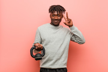 Young fitness black man holding a dumbbell showing victory sign and smiling broadly.