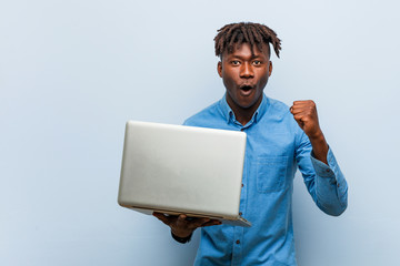 Young rasta black man holding a laptop cheering carefree and excited. Victory concept.