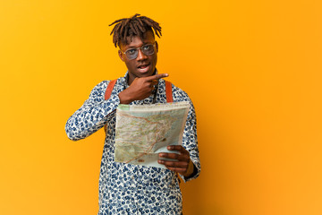 Young rasta black man holding a map smiling cheerfully pointing with forefinger away.