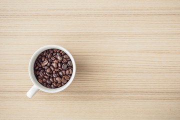 fresh roasted coffee beans in white cup on wood table, top view