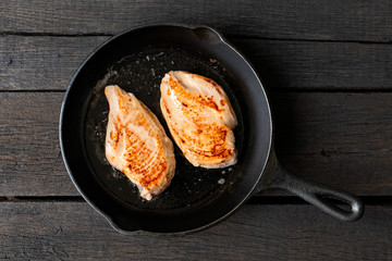 Two whole chicken breasts roasting in cast iron pan isolated on dark wood. Top view.