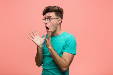 Young cool caucasian man shouts loud, keeps eyes opened and hands tense.