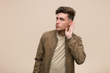 Young caucasian man wearing a brown jacket trying to listening a gossip.