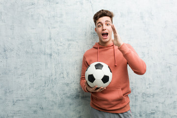 Young sporty man holding a soccer ball shouting excited to front.