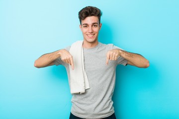 Young fitness teenager man points down with fingers, positive feeling.