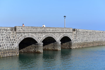 Fototapeta na wymiar People on the Puente de las Bolas, drawbridge in front of the fort of Castillo de San Gabriel, Arrecife, Lanzarote, Canary Islands, Spain 