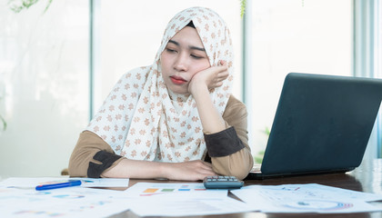 Tired confused bored and headache Thai young muslim woman worker or businessman wearing hijab while reading graph and chart report documents.