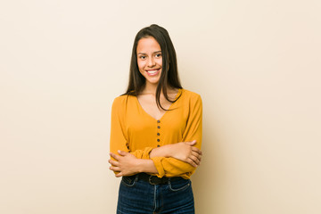 Young hispanic woman against a beige background who feels confident, crossing arms with determination.