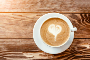 Cappuccino coffee cup with heart shaped foam on a wooden table in cafe