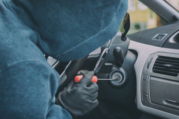 Hooded thief sits in the car and tries to break the ignition switch