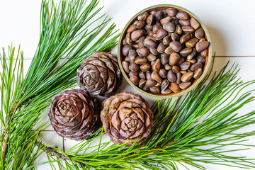 Cedar cone, nuts and a branch of Siberian cedar on a light wooden background. The concept of wholesome food, organic food, vegetarianism. Top view, place for text. Pignolia nuts