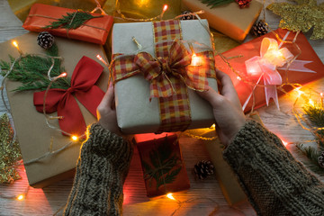 hands holding a Christmas gift with a background of lights and more gifts