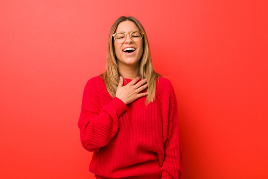 Young authentic charismatic real people woman against a wall laughs out loudly keeping hand on chest.