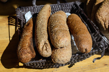 Five whole-grain bread sticks displayed for sale in a black plastic basket at a street food market, selective focus