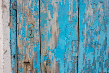 Part of an old wooden door with peeling blue paint and a keyhole