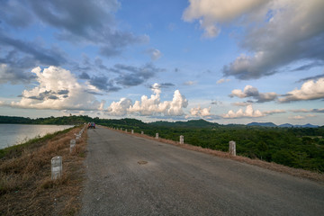 long concrete road with short pole beside with green mountain and beautiful cloudy blue sky background.